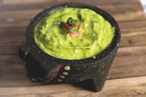 Guacamole in a black stone molcajete on a wooden tabletop